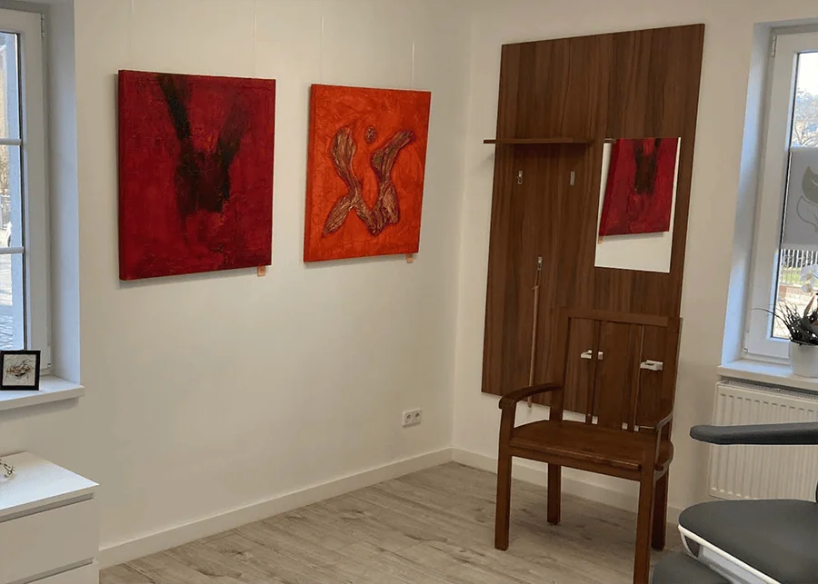 Zwei rote Gemälde an einer Wand in einem Raum mit einem Holzstuhl und einem Spiegel.